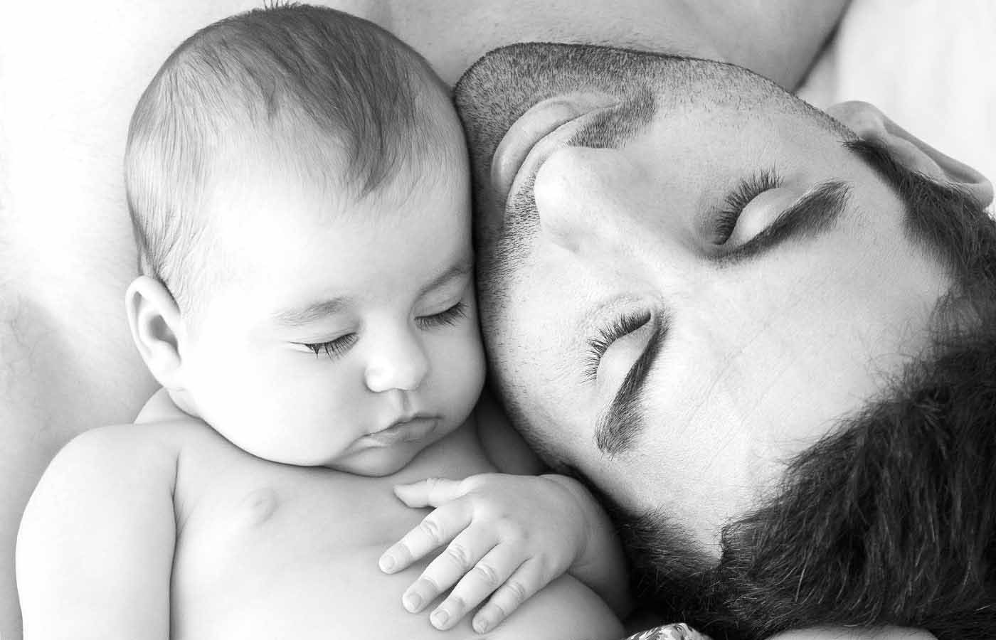 A black and white photograph of a father snuggling cheek to cheek with his newborn baby taken by Jessica Loren in her Brisbane studio.